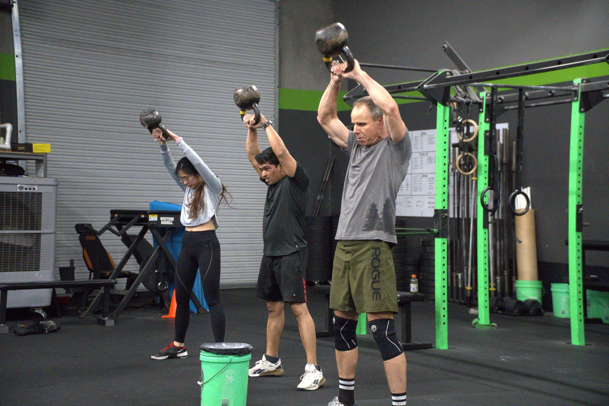 Three members pressing kettlebells overhead together in a group class at El Dorado Hills CrossFit
