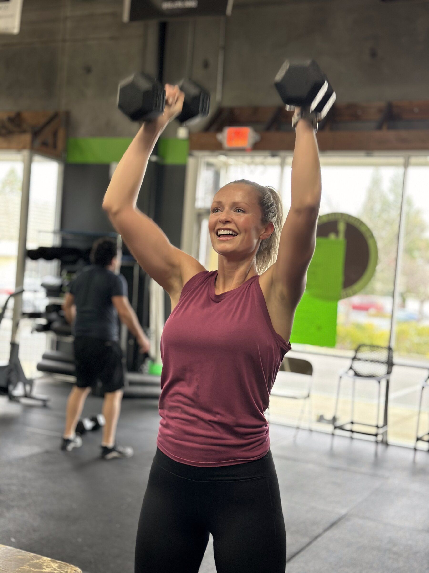 Smiling member pressing dumbbells overhead during a class at El Dorado Hills CrossFit